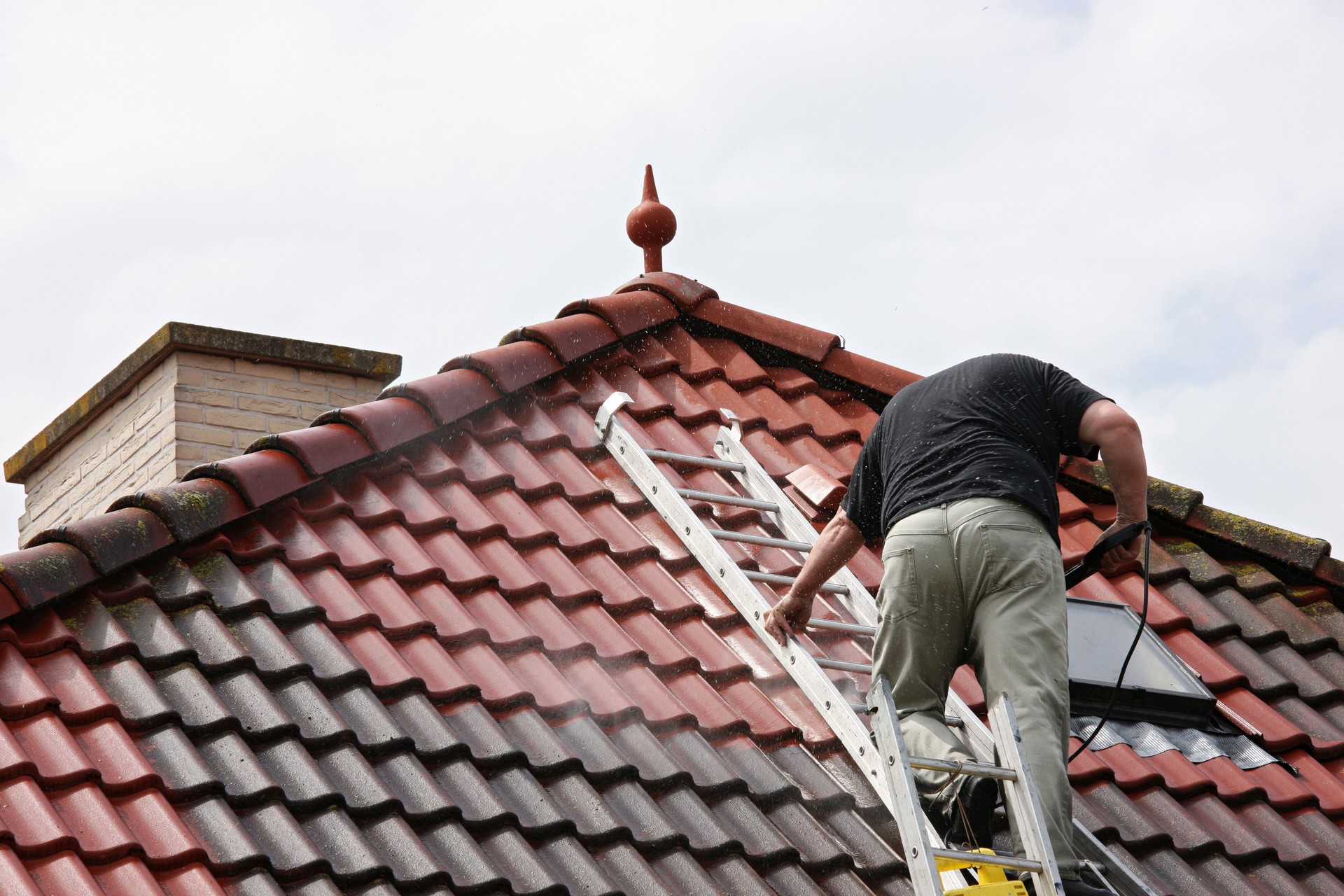 Man on a roof, cleaning the tiles with pressure washer